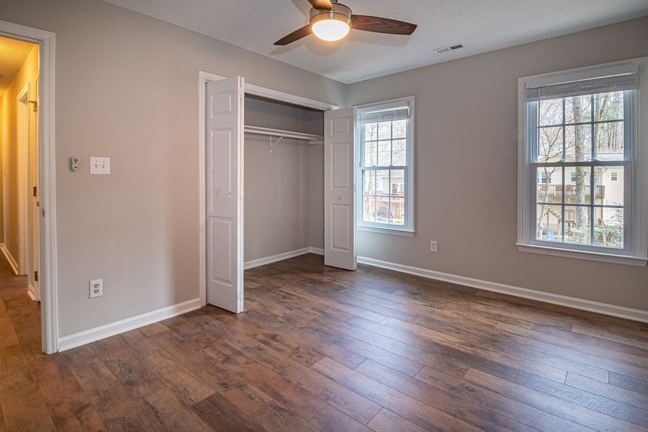 A spacious, well-lit bedroom featuring a hardwood floor with a polished, smooth surface. The room has light gray painted walls and two large double-glazed windows with white frames, allowing natural d