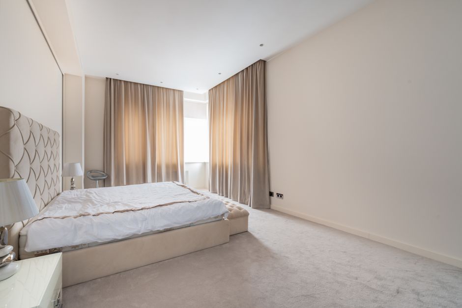 A spacious, well-lit bedroom featuring a hardwood floor with a polished, smooth surface. The room has light gray painted walls and two large double-glazed windows with white frames, allowing natural d